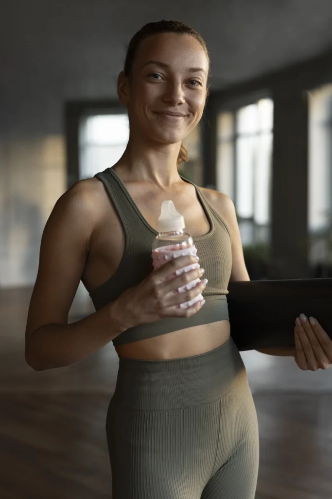 Zdjęcie kobiety w stroju sportowym, trzymającej butelkę z wodą - fitness jako profilaktyka antycellulitowa.
