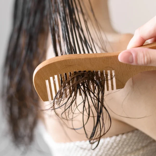 Kobieta wczesuje podkład pod olejowanie włosów drewnianym grzebieniem